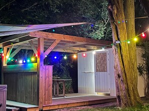 Una terraza de madera con un pérgola, un jacuzzi y luces colgantes.