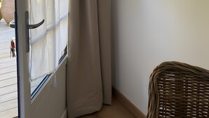 Una habitación con puerta corrediza de vidrio, una silla de mimbre y una pared blanca.