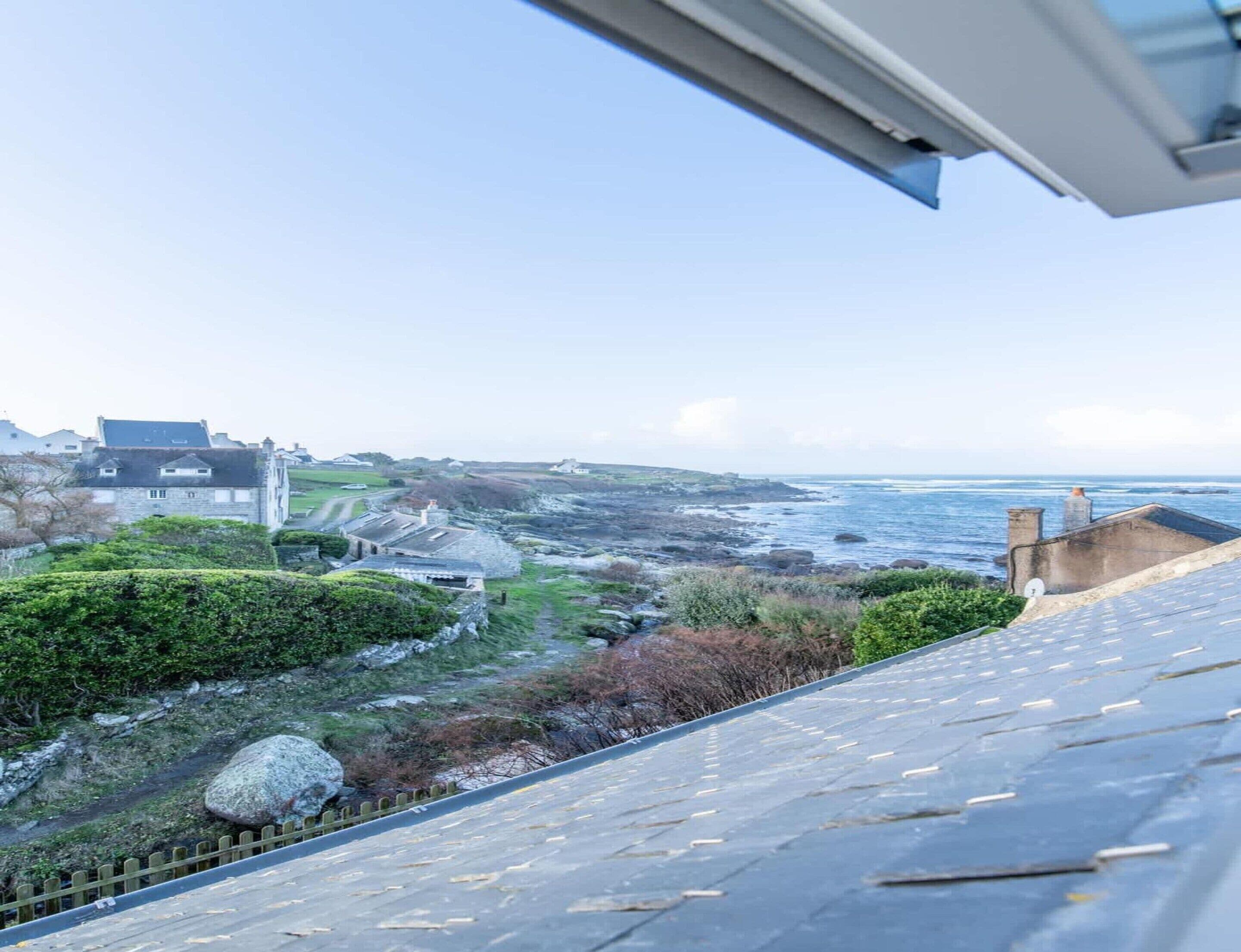 A coastal view with buildings, a paved path, and a rocky shoreline.