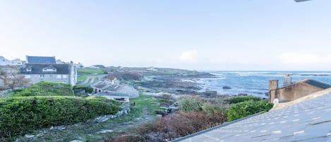 A coastal view with buildings, a paved path, and a rocky shoreline.