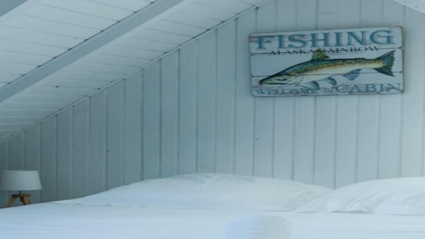 A cabin interior with a bed, towels, and a sign indicating it's a fishing cabin in Alaska. - House in Porspoder by Plage du Bourg Beach (Porspoder)