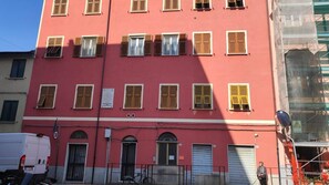 A multi-story building with a red facade, multiple windows with shutters, and a sign indicating a public space. - Apartment 'Residenza Vittoria - 1' with Wi-Fi and Air Conditioning (La Spezia)