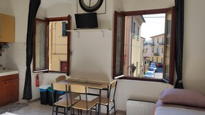 A small room with a table, chairs, a bed, a TV, and a window with a view of a street. - Apartment 'Residenza Vittoria - 1' with Wi-Fi and Air Conditioning (La Spezia)