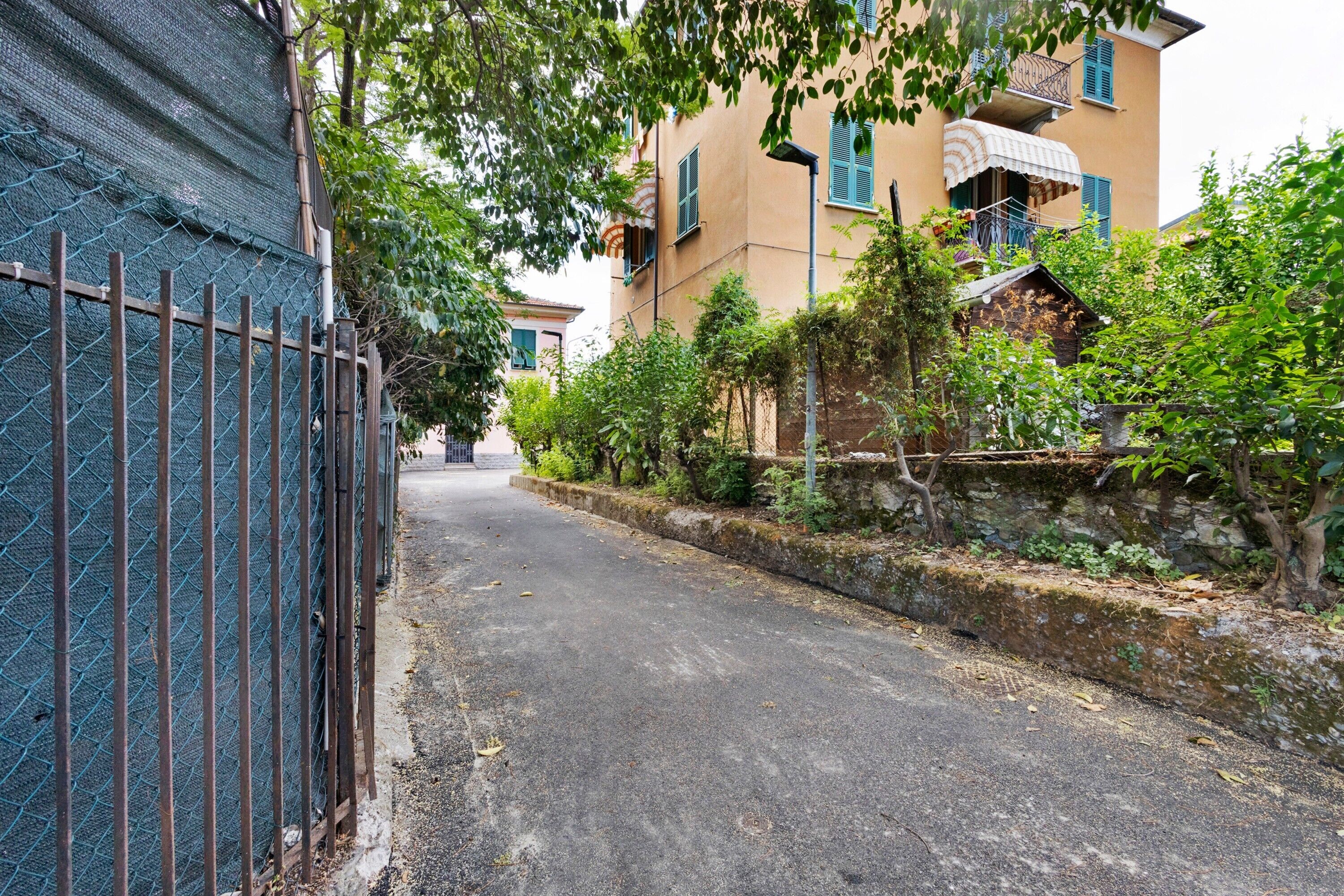 Une rue étroite bordée d’immeubles dotés de balcons, d’une clôture en métal et de verdure.