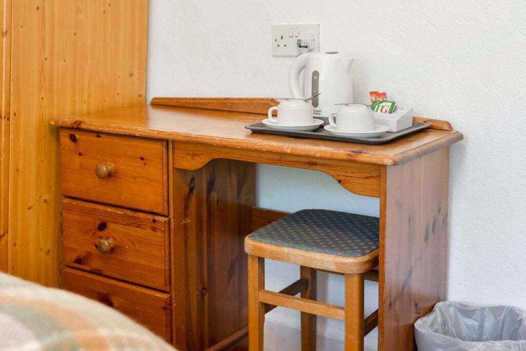 A wooden desk with a tray holding a coffee maker, cups, and a box of tissues.