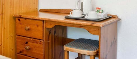 A wooden desk with a tray holding a coffee maker, cups, and a box of tissues.