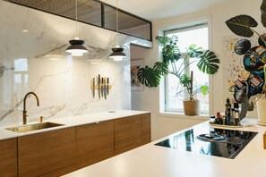 Eine moderne Küche mit Marmorarbeitsplatte, Holzschränken, einem eingebauten Backofen und Pendelleuchten.