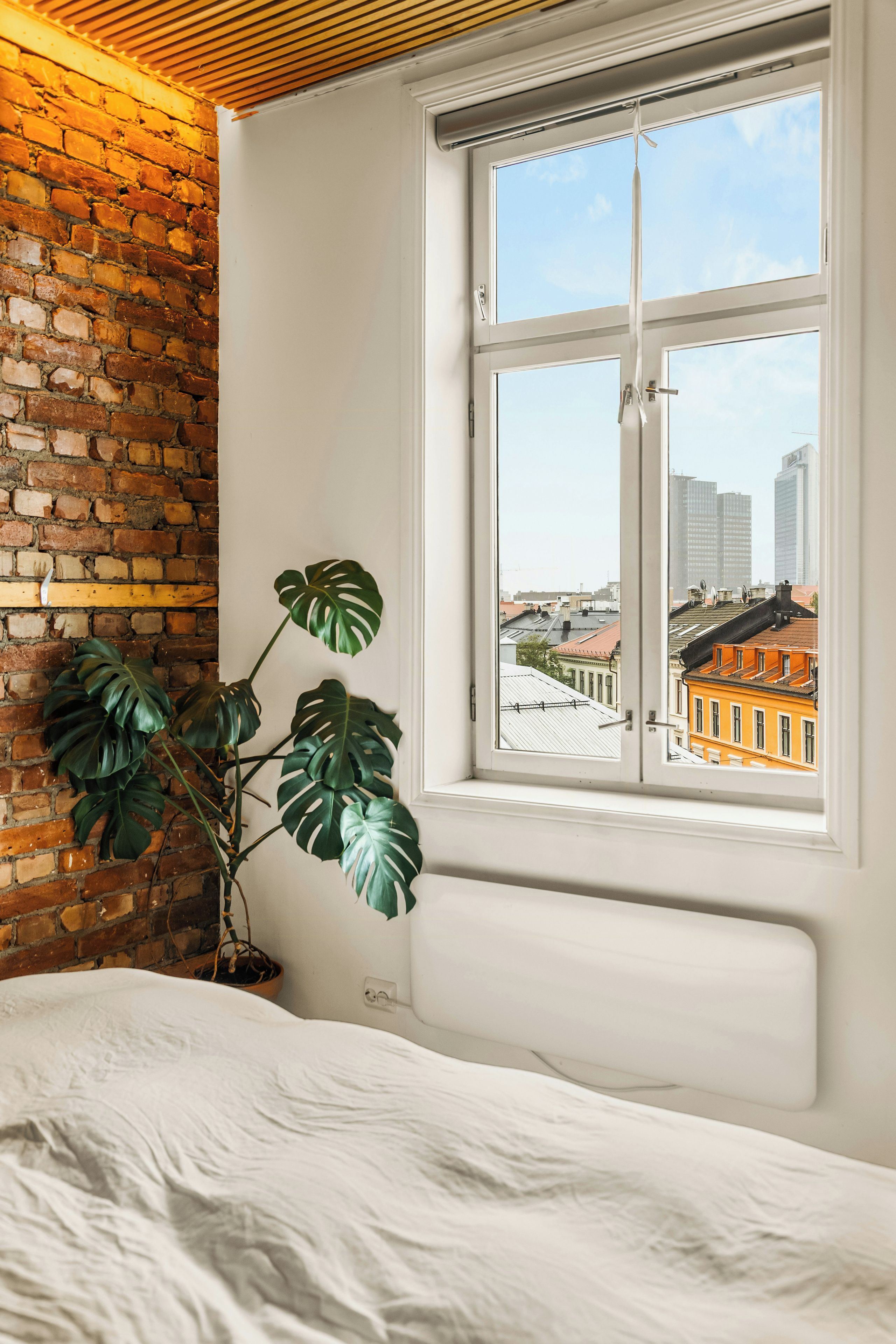 Une pièce avec un mur en briques, une fenêtre donnant sur des immeubles et une plante en pot.