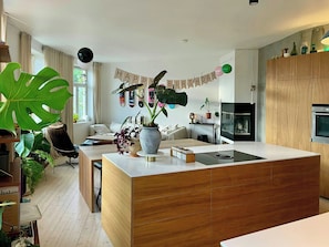 A modern kitchen with a central island, wooden cabinets, and a dining area with a chair and table. - Light apartment with rooftop views in Tøyen (Oslo)