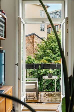 Blick von einem Balkon mit Tisch und Stühlen, einer Ziegelwand und einem Gebäude im Hintergrund.