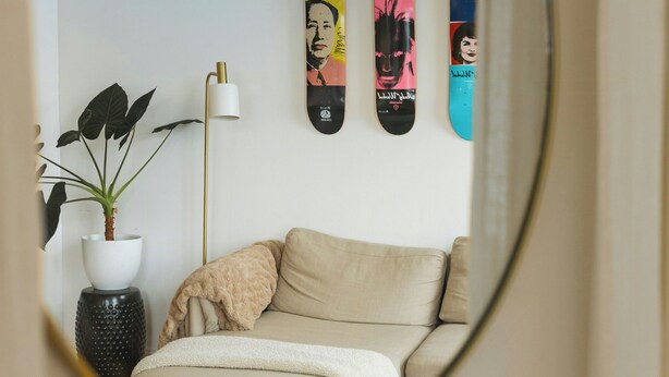 A mirror reflecting a room with a bed, a potted plant, a lamp, and three skateboards on the wall. - Light apartment with rooftop views in Tøyen (Oslo)