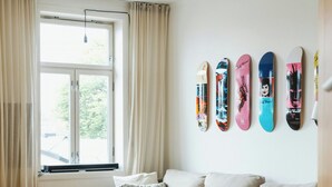 A modern living room with a sofa, ottoman, and a coffee table. There is a window with curtains, and a wall with skateboard art. - Light apartment with rooftop views in Tøyen (Oslo)