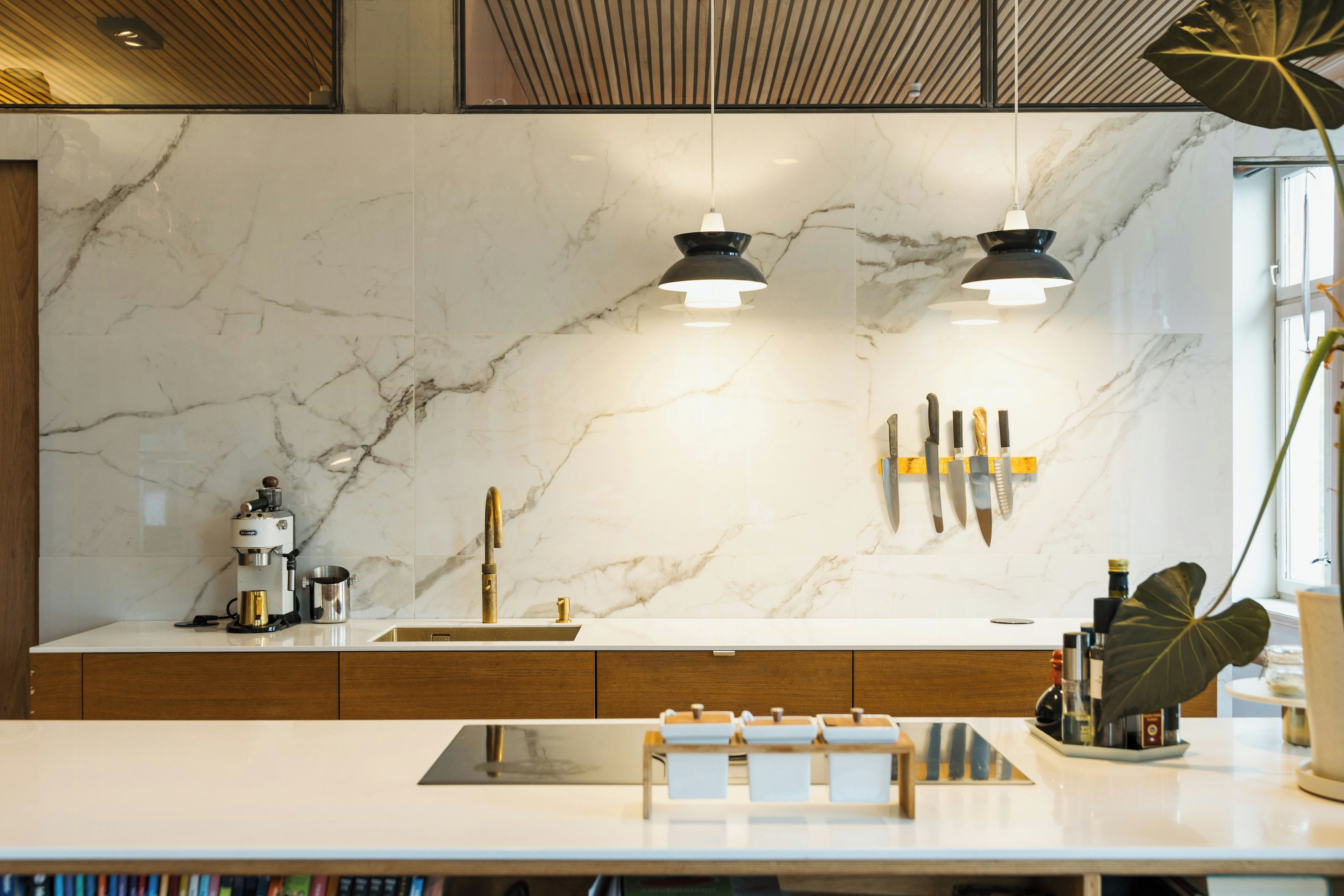 Una cocina moderna con salpicadero de mármol, iluminación colgante y una cafetera.