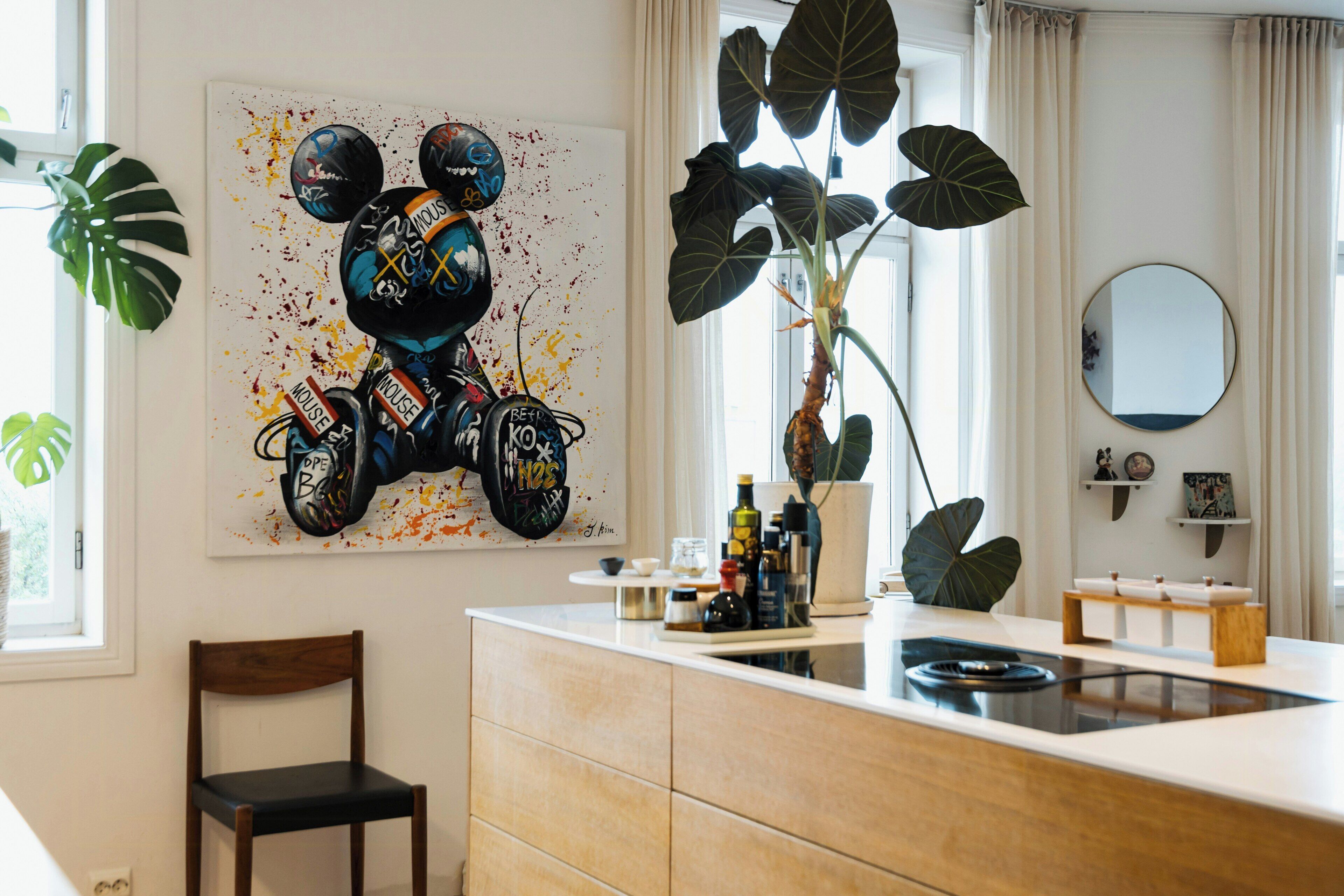 A modern kitchen with a central island, a dining area with a chair, and a large wall painting.