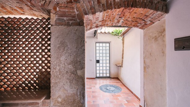 Un corridoio stretto con pavimento piastrellato, un arco in mattoni e una porta con inferriata.