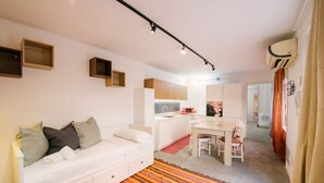 Un ambiente compatto con un divano bianco, un tavolo da pranzo, una zona cucina e un tappeto decorato.