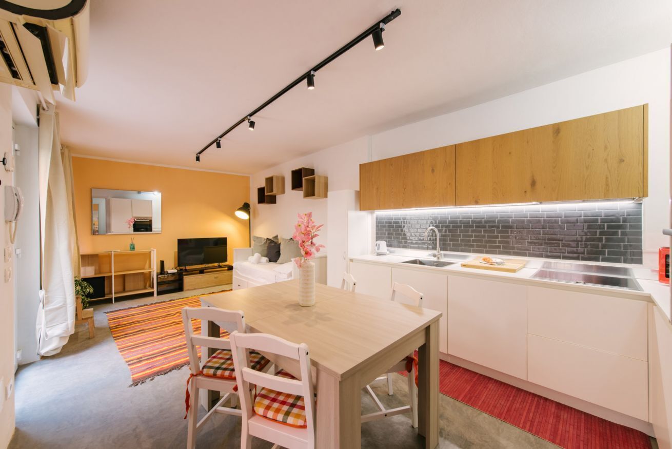 A modern kitchen with white cabinets, a wooden dining table, and a red rug.