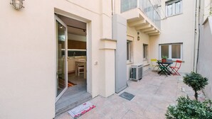 Un edificio residenziale con un ingresso con porta in vetro, un piccolo patio con tavolo e sedie, e una pianta in vaso.