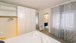 Camera d'albergo con un letto, un armadio, e un bagno parzialmente visibile attraverso una porta aperta, con tende decorate.