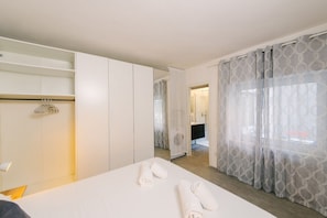 A hotel room with a bed, a wardrobe, a bathroom visible through an open door, and patterned curtains. - Scalone XVI Ottobre | Dimora con cortile privato (Verona)