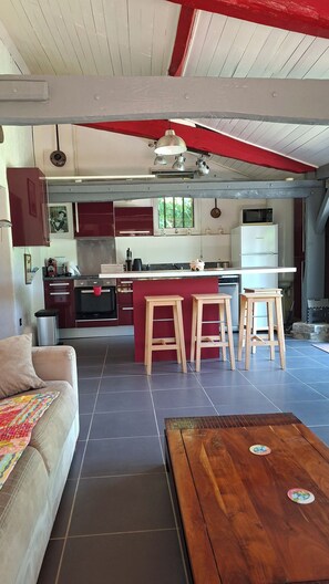 Eine moderne Küche mit einer zentralen Kochinsel, Holzbarhocker und einem Essbereich mit Sofa und Couchtisch.