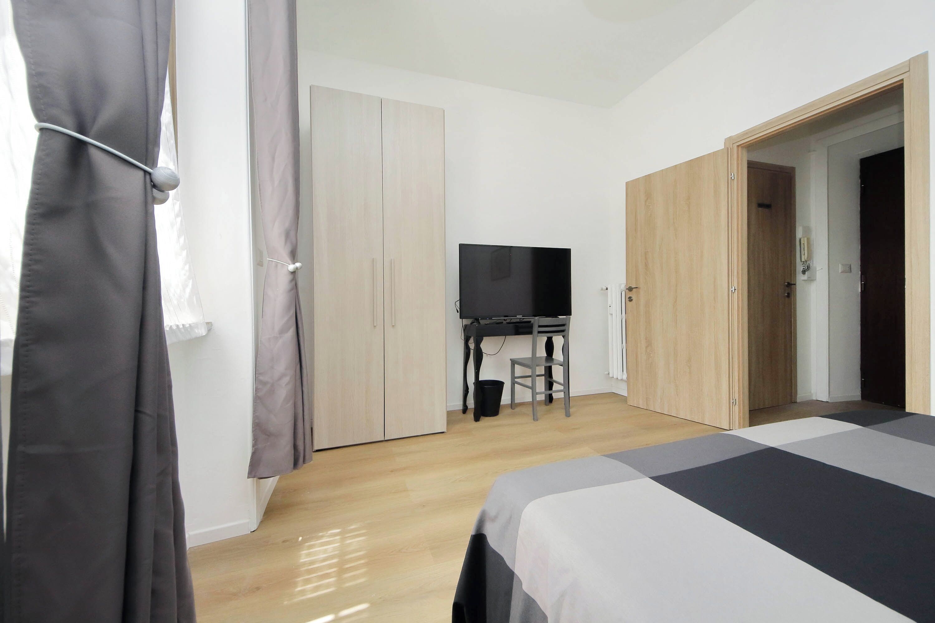 A bedroom with a bed, a TV, a desk, and a wardrobe.