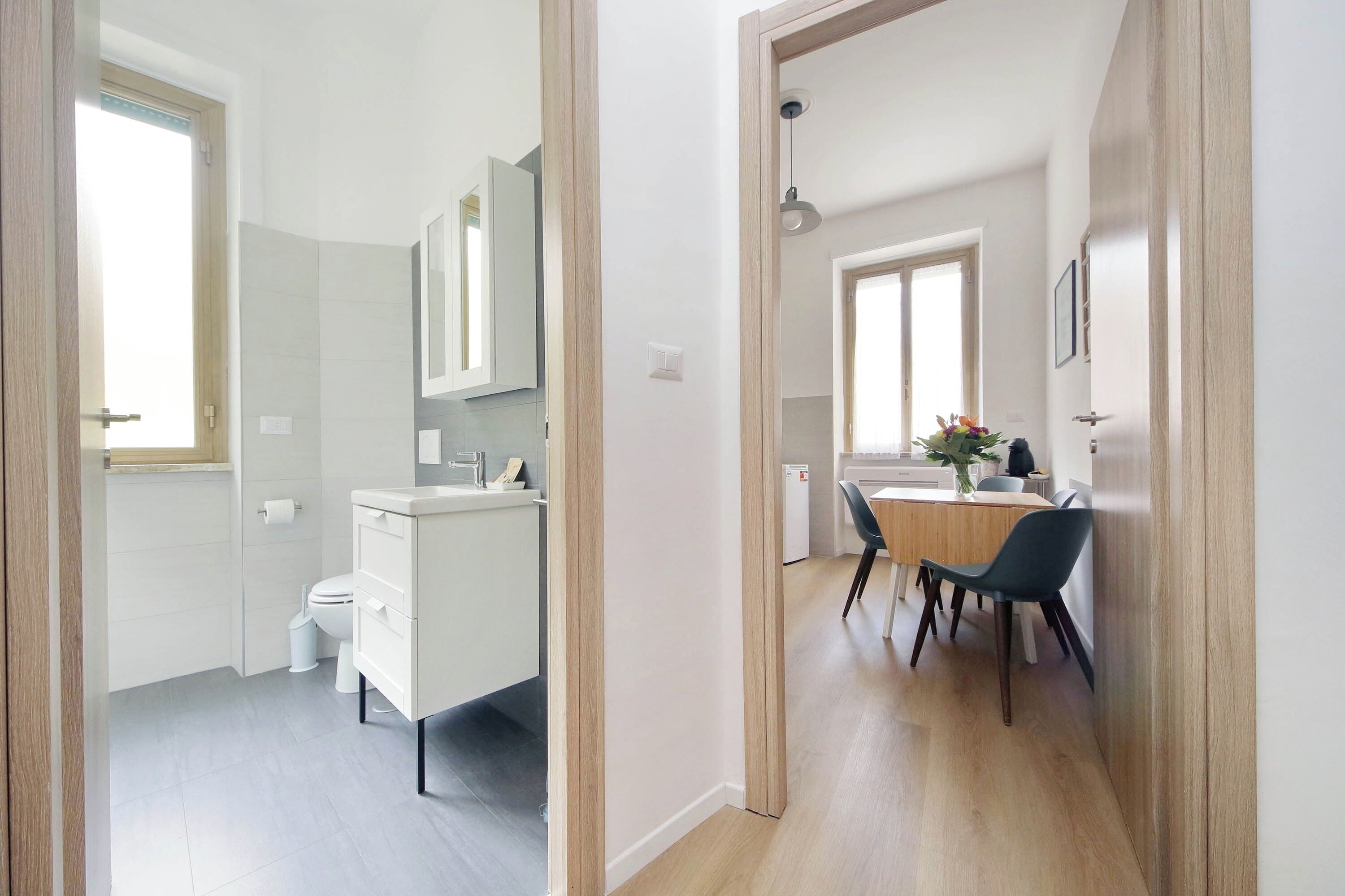 A modern kitchen with a built-in oven, a dining area with a wooden table and chairs, and a bathroom with a toilet and sink.