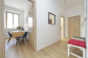 A room with a dining table, chairs, a bed with a red blanket, a wooden door, and a mirror on the wall. - 4BNB - DAquino Apartment close to Vatican Museums (Rome)