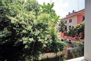 A balcony with dense foliage, a building with balconies, and a clear sky. - 4BNB - DAquino Apartment close to Vatican Museums (Rome)