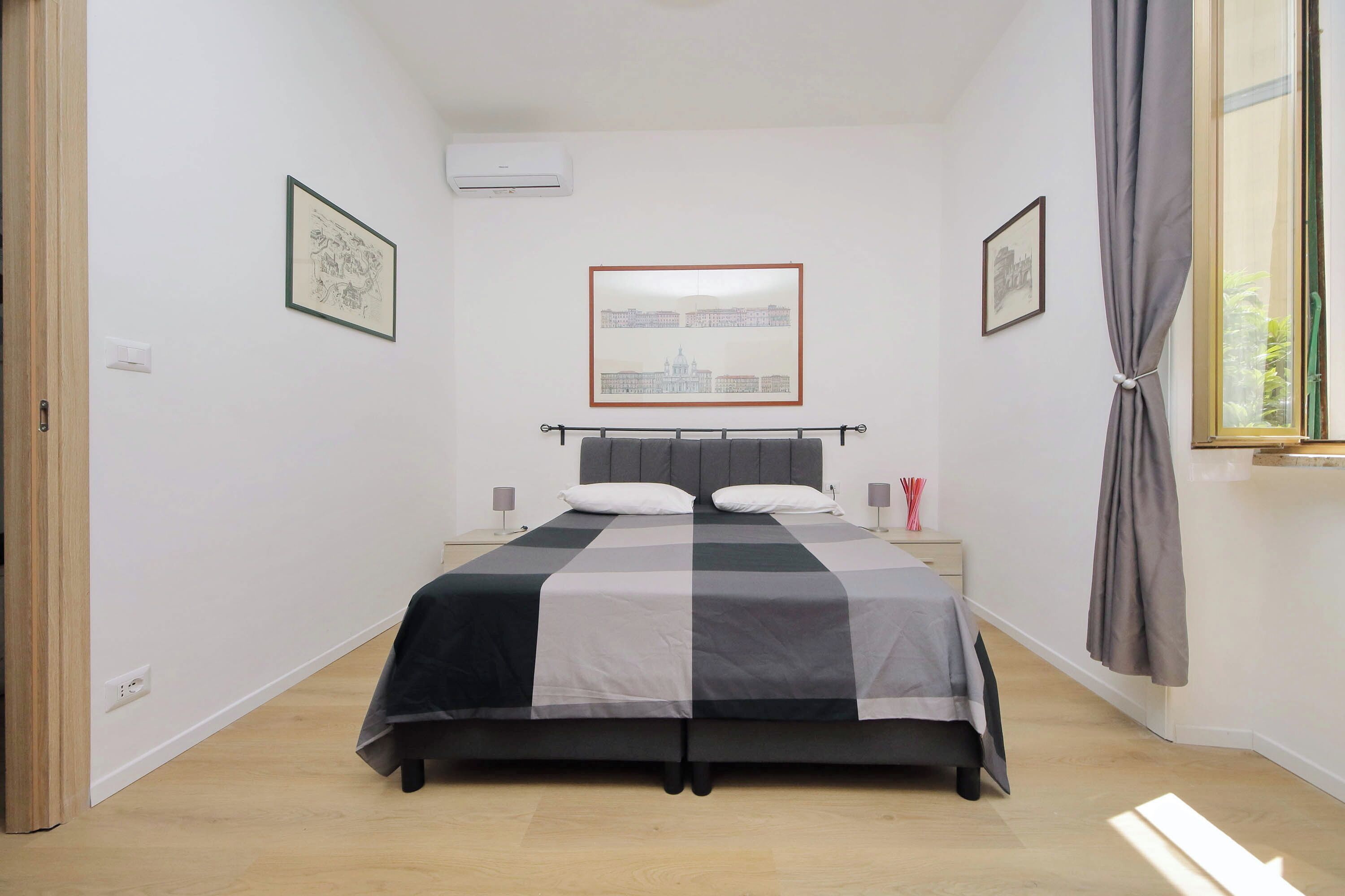 A bedroom with a bed, a window with curtains, and wall-mounted artwork.