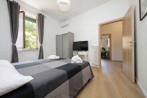 A hotel room with a bed, a desk with a TV, a wardrobe, and a door leading to another room. - 4BNB - DAquino Apartment close to Vatican Museums (Rome)
