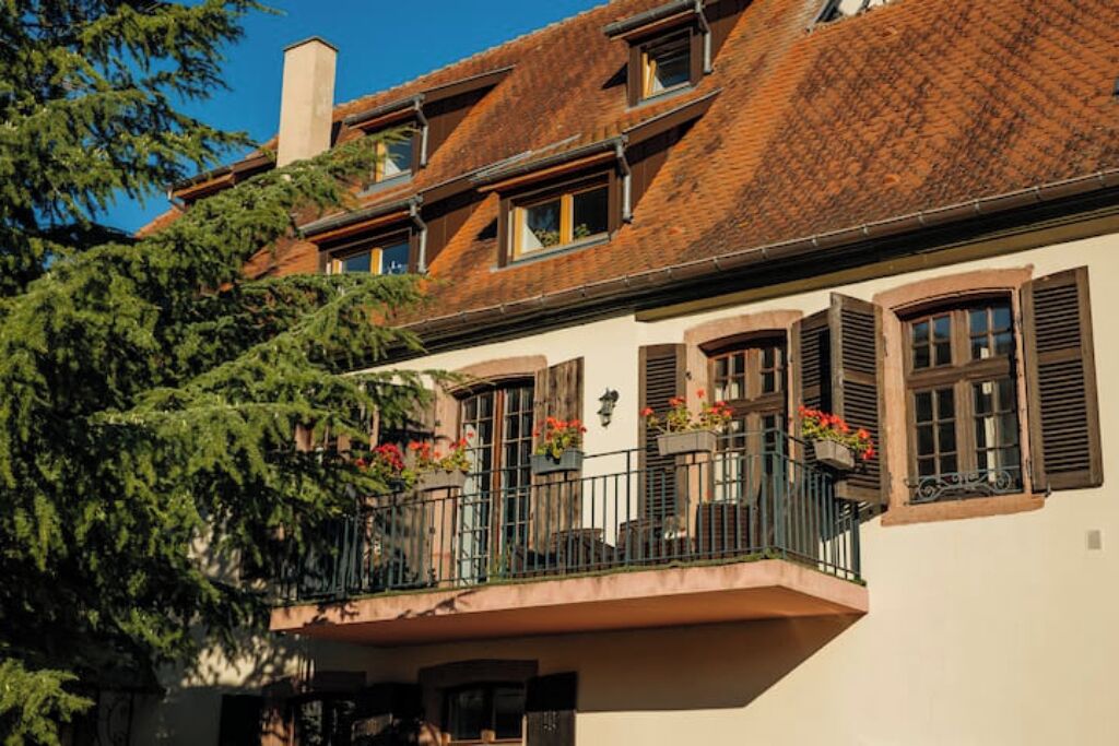 A traditional European-style building with a balcony, windows with shutters, and a chimney.