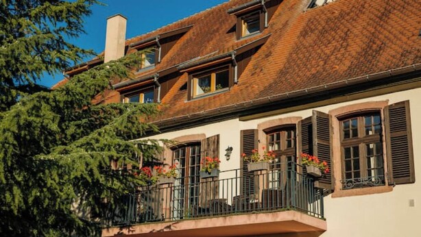 Un edificio de estilo europeo tradicional con balcón, ventanas con contraventanas y una chimenea.