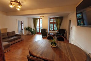 A spacious living room with a wooden dining table, comfortable seating, and large windows with curtains. - La Cure Apartment (Wintzenheim)