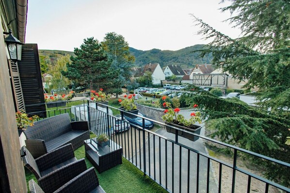 A balcony with outdoor furniture and potted plants, overlooking a parking area and buildings with traditional architecture. - La Cure Apartment (Wintzenheim)
