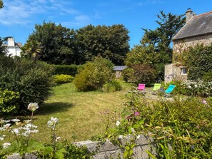 A garden with a lawn, a stone wall, and a small building with a chimney. - Charming Coastal Stone House With Garden (Landunvez)
