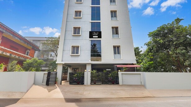 Un hotel de varios pisos con una entrada central, un letrero y un camino de acceso con portones.
