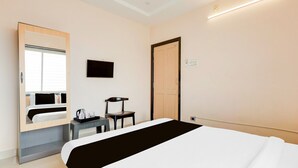 Una habitación de hotel con una cama, un escritorio con silla, un televisor y una puerta.