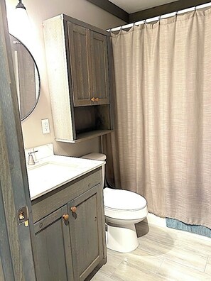 A bathroom with a toilet, a sink, a mirror, and a shower curtain. - Welcome to Little Bit O' the Bay (Saint Leonard)