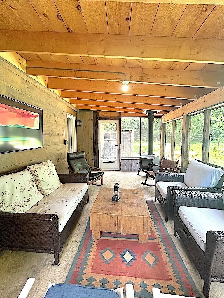 Interior acollidor d'una cabana amb sostre de fusta, mobles de vimet i una finestra gran que dona a la vegetació.