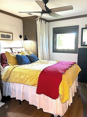 A bedroom with a bed, a ceiling fan, a window, and a nightstand. - Welcome to Little Bit O' the Bay (Saint Leonard)
