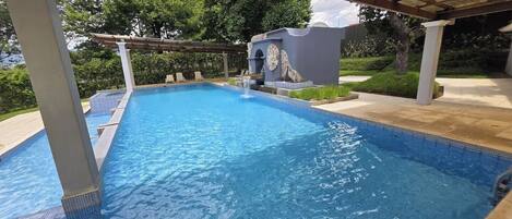 Una piscina cristalina con una pérgola encima, rodeada de follaje.