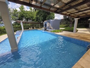 Ein klares Schwimmbecken mit einer Pergola darüber, umgeben von Grünpflanzen.