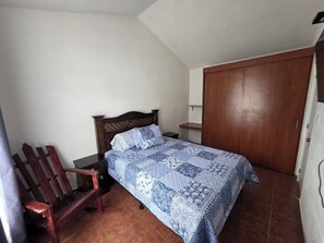 Ein Schlafzimmer mit Bett, Holzstuhl, Nachttisch und Kleiderschrank.