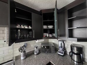 A kitchen with dark cabinets, a granite countertop, a coffee maker, and a kettle. - Just 15 minutes from Antigua Guatemala, within the La Joya Condominium. (Santa Lucía Milpas Altas)