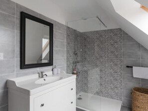 A modern bathroom with a white vanity, a large mirror, patterned tiles, and a shower. - Charming Coastal Home in Landunvez (Landunvez)