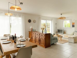 A modern kitchen with wooden cabinets, a dining table set for four, and pendant lighting. - Charming Coastal Home in Landunvez (Landunvez)