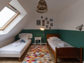 Ein Zimmer mit zwei Betten, einem kleinen Tisch, einer Lampe, einer Pendelleuchte und einem geometrisch gemusterten Boden.