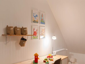 Ein Spielbereich für Kinder mit einem Holztisch, Spielzeug, einer Lampe und Bildern an der Wand.