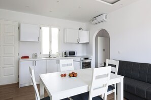 Eine moderne Küche mit weißen Schränken, einer Mikrowelle und einem Toaster. Es gibt einen Esstisch mit Stühlen und ein dunkelgraues Sofa.